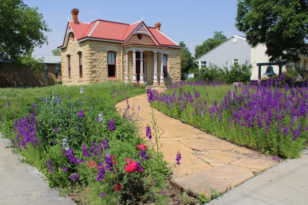 Little limestone museum with wild flowers and limestone sidewalk.