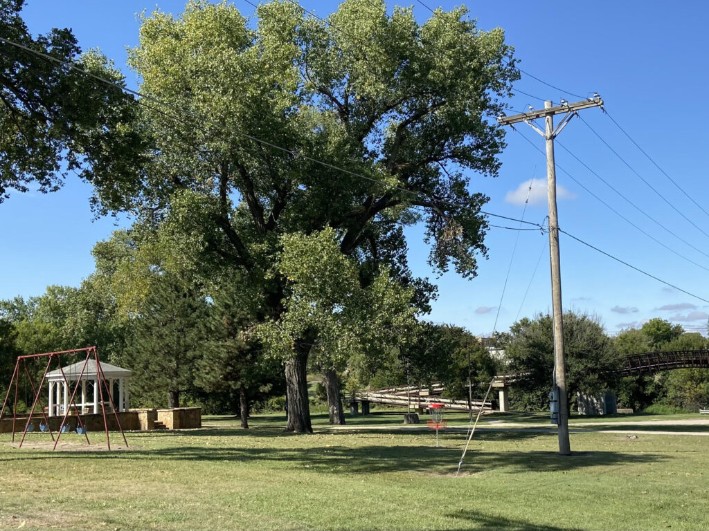 Park view with gazebo, swing set, disc golf, and bridge.