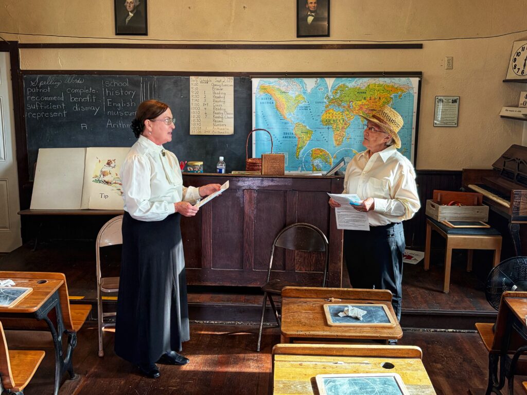A schoolmarm and farmer talking at the front of a one-room schoolhouse