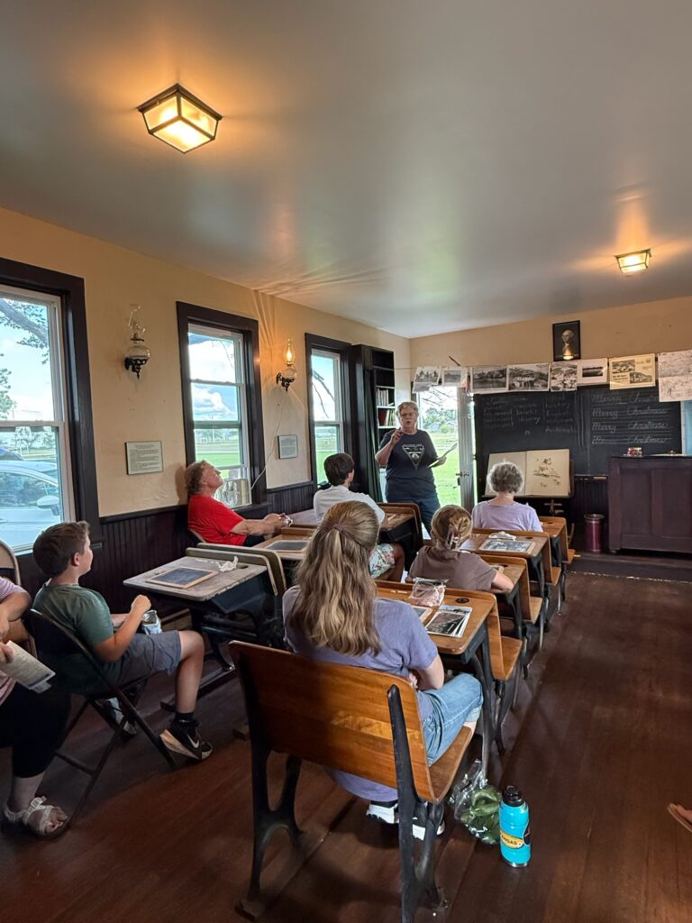 A women teaching a group at a one-room schoolhouse