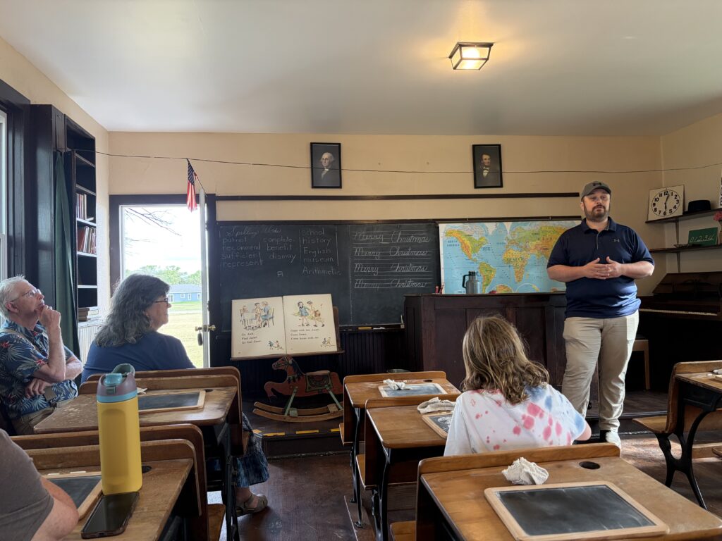 A man talking at the front of a one-room schoolhouse