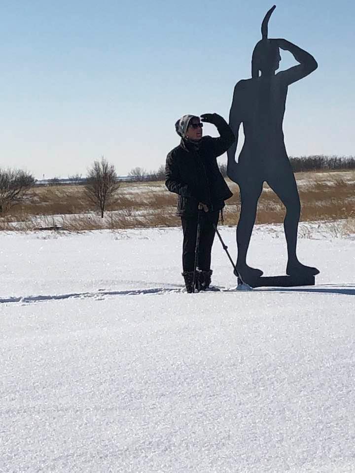 A lady hiking in winter standing next to a Native American statue