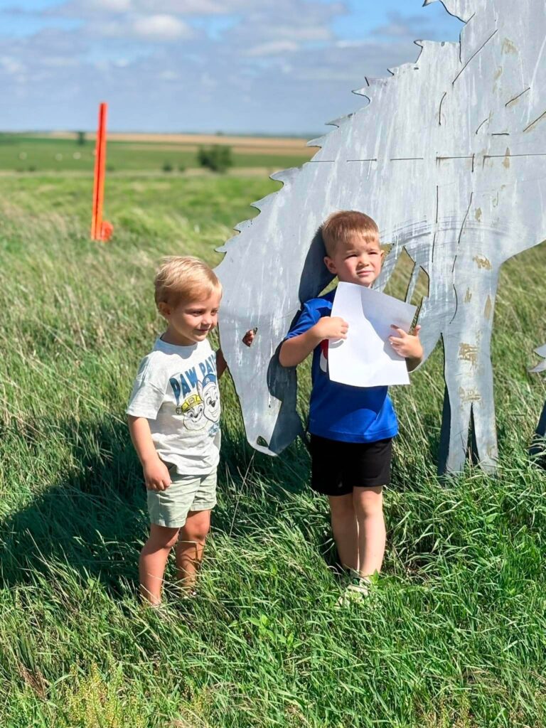 Two toddler boys standing in front of a metal cutout of a horse